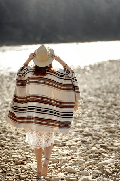 Photo beautiful woman traveler wearing hat and poncho walking at river beach american outfit boho concept space for text