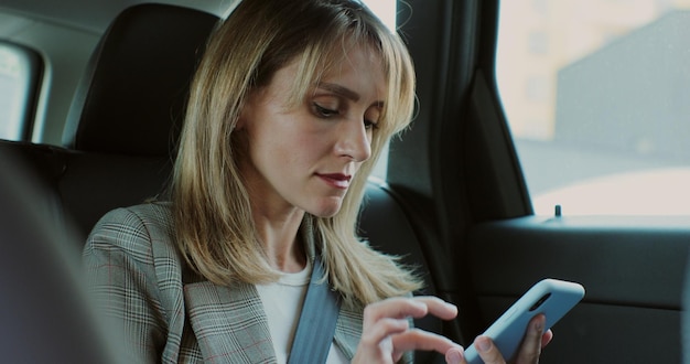 Bella donna che digita sul suo smartphone in macchina signora manager che guarda il telefono sul sedile posteriore di un'auto