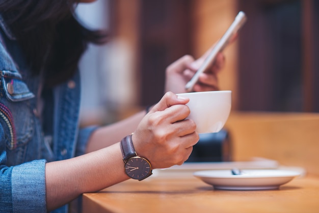 Messaggio di battitura a macchina della bella donna sullo smart phone in un caffè