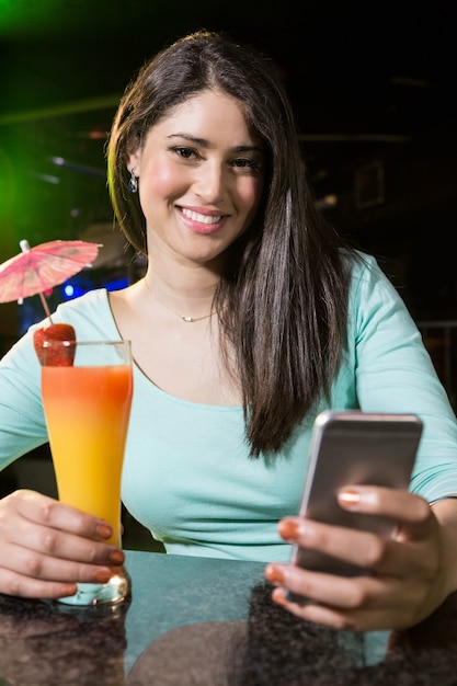 バーカウンターでカクテルを飲みながらテキストメッセージを入力する美しい女性