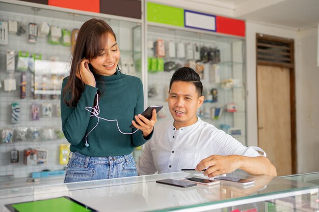 A beautiful woman using earphones and a mobile phone beside a male shop assistant