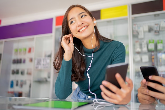 A beautiful woman using earphones while using a mobile phone near a display case