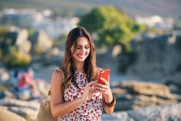 Bella donna che utilizza lo smartphone che manda un sms sulla spiaggia al tramonto