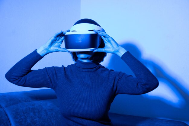 青い光の中で自宅の仮想空間でvrヘッドセットを使用して美しい女性。仮想世界の概念。仮想空間でのライフスタイル