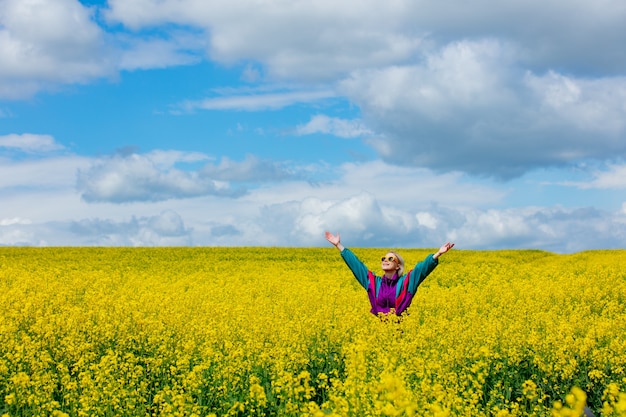 Beautiful woman in vintage tracksuit in yellow rapeseed field