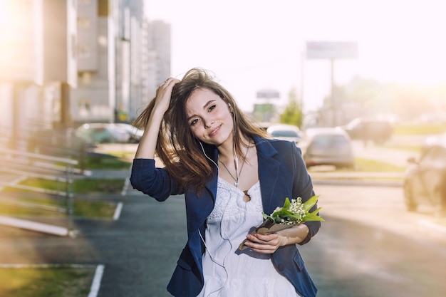 아름 다운 여자는 그의 손에 백합 꽃다발과 함께 헤드폰에서 음악을 듣고 도시 주위를 산책