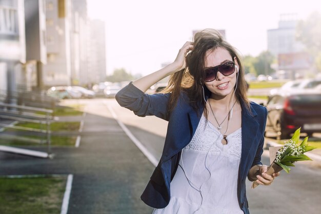 Beautiful woman walks around the city listening to music in headphones with a bouquet of lilies in his hands