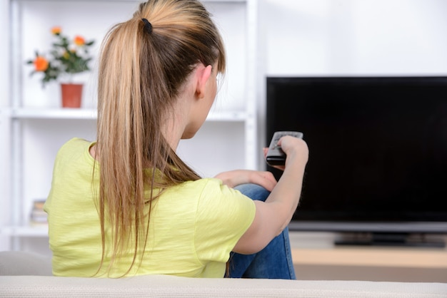 Bella donna che guarda tv seduto sul divano di casa.