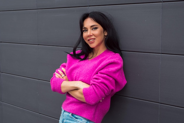 Beautiful woman wearing bright pink sweater posing on dark gray background at city street