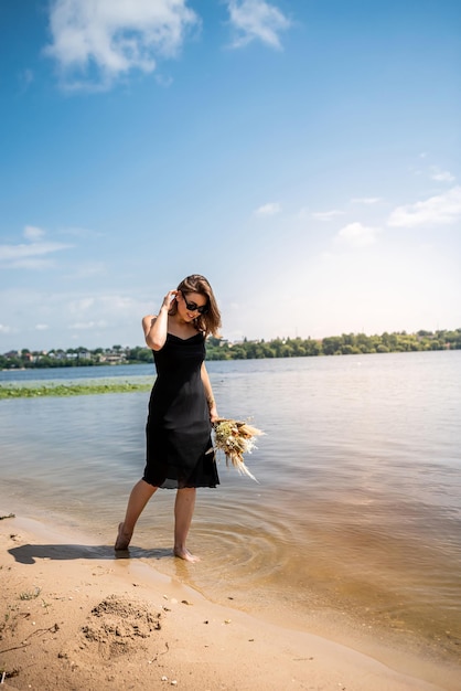 Beautiful woman wearing coctail black dress standing on water lake