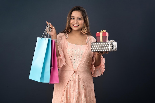 Beautiful woman wearing Indian traditional dress holding shopping bags and gift Box on a grey background