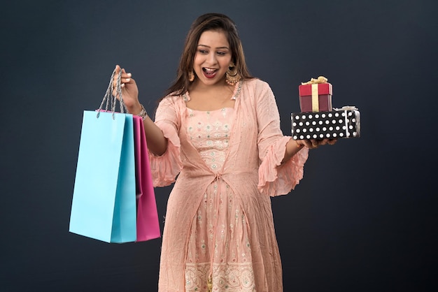 Beautiful woman wearing Indian traditional dress holding shopping bags and gift Box on a grey background
