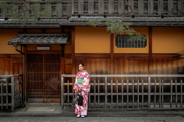 Beautiful woman wearing kimono standing in front of the wooden traditional house in Kyoto,