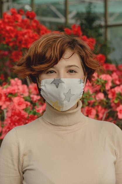 Una bella donna che indossa una maschera protettiva tra i fiori primaverili. concetto di pandemia di coronavirus