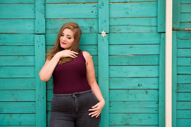 Beautiful woman wearing ripped jeans standing against cafe wall on city street. Casual fashion, elegant everyday look. Plus size model.