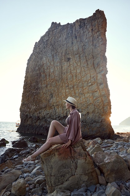 Beautiful woman wearing a straw hat on the beach in the style of light maroon and dark gray dreamy and romantic compositions stone sculptures mountain