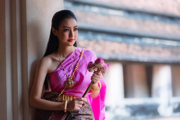 Фото Красивая женщина в традиционной одежде с цветами в руках, стоя у стены