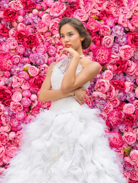 Красивая женщина в свадебном платье на цветочной стене