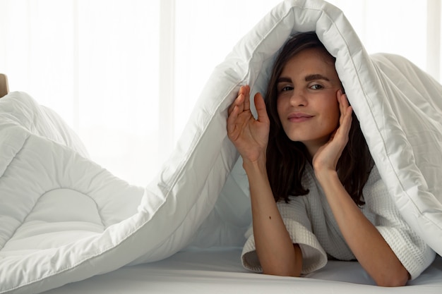 Beautiful woman under a white blanket on the bed.