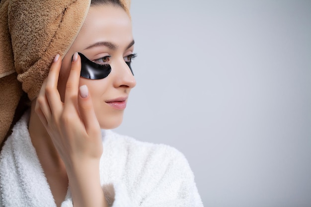 Beautiful woman in a white coat applies patches to the eyes for skin care.