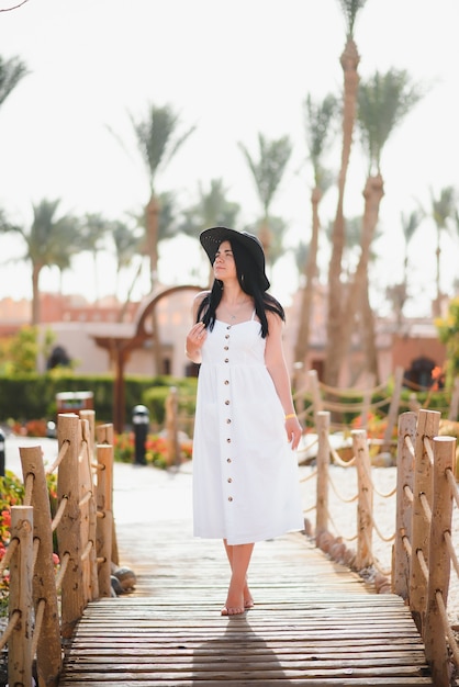 Beautiful woman in white dress and a black hat walking around a luxury hotel