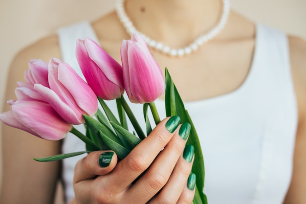 Bella donna in abito bianco e collana di perle in possesso di un tulipani rosa