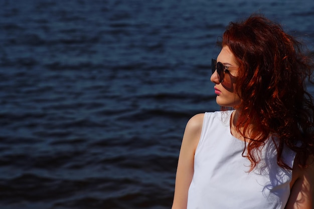 하얀 드레스와 선글라스를 입은 아름다운 여성이 배경에 깊고 푸른 물 야외에서