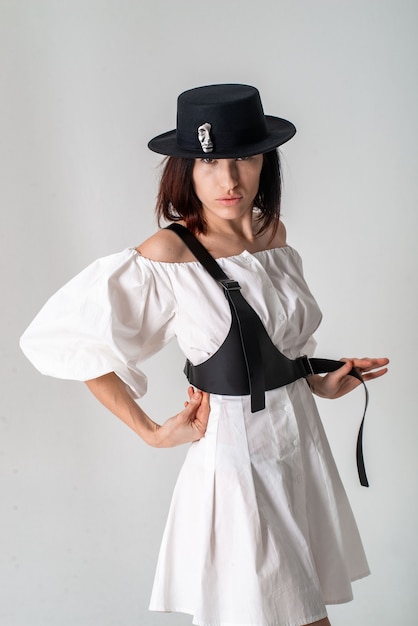 Beautiful woman in a white short dress, hat and harness on a white background