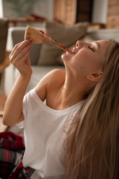 La bella donna in una maglietta bianca mangia la pizza con piacere