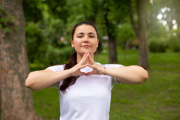 Beautiful woman in white t-shirt shows mudra in folded fingers outdoor