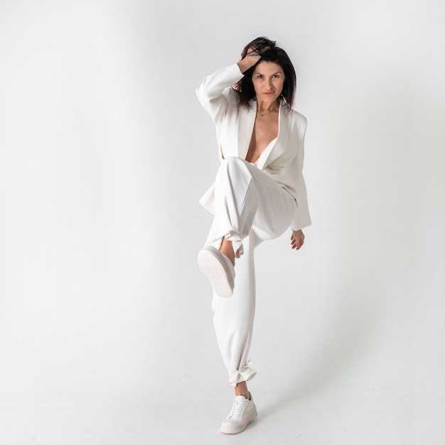 Beautiful woman in a white trouser stylish suit and white shoes on a white background