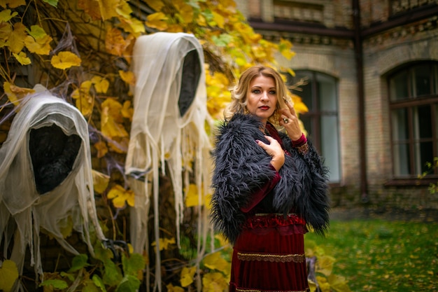 Beautiful woman in a witch costume stands on a background of ghosts. Stylized Halloween decor.