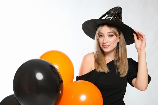Beautiful woman in witch costume with balloons on white background Halloween party