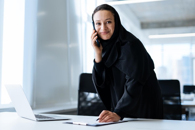 Beautiful woman with abaya dress working on her computer. Middle aged female employee at work in a business office in Dubai. Concept about middle eastern cultures and lifestyle