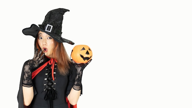 Beautiful woman with black and orange hair in black dress and witch hat is holding pumpkin with wow emotion Halloween concept