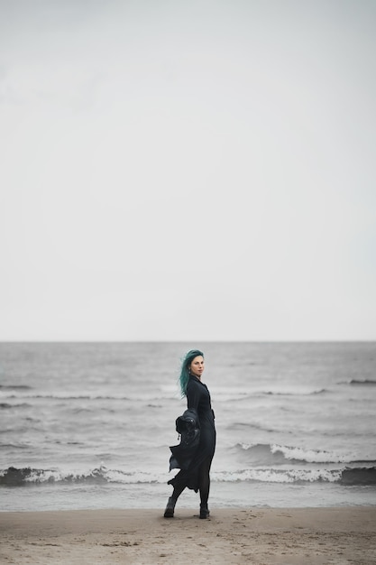 La bella donna con capelli blu cammina lungo la riva del mare e gode del vento