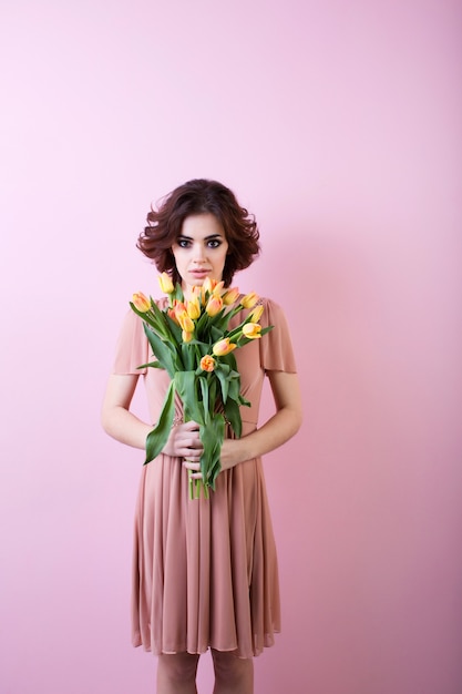 Beautiful woman with a bouquet of flowers over pink background.