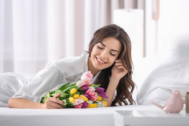 Beautiful woman with bouquet of tulips on bed at home