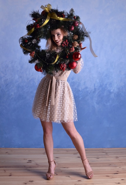 Beautiful woman with christmas wreath in hands on blue background