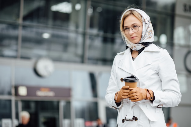 事務所ビルの近くのコーヒーカップを持つ美しい女性。