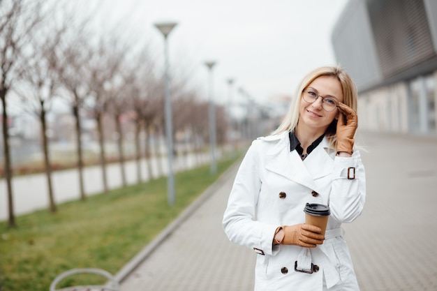 Beautiful woman with coffee cup near office building.