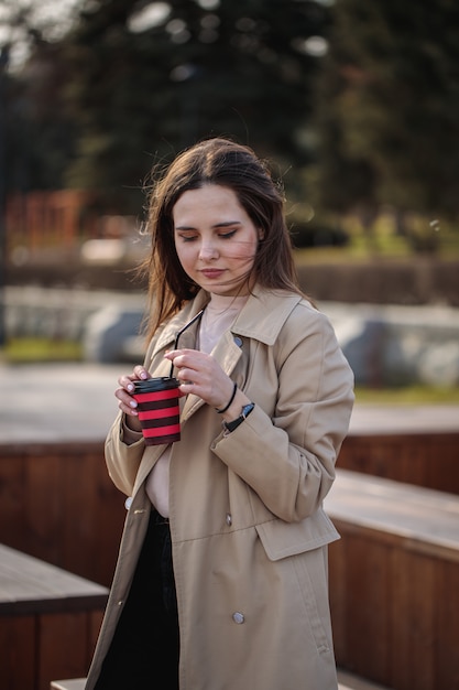 Beautiful woman with coffee in hand walks in sunny weather around the city