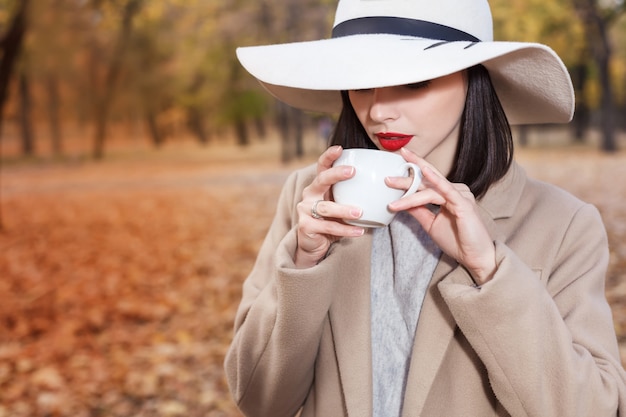 秋の公園でコーヒーカップを持つ美しい女性