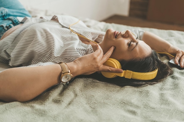 Foto una bella donna con i capelli scuri è sdraiata sul letto a casa con le cuffie