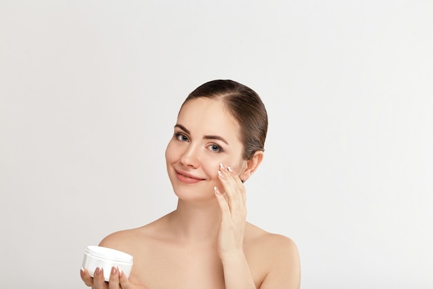 Foto bella donna con crema per il viso. protezione della pelle. cura della pelle. spa. una giovane donna tiene crema idratante e sorridente. trucco naturale