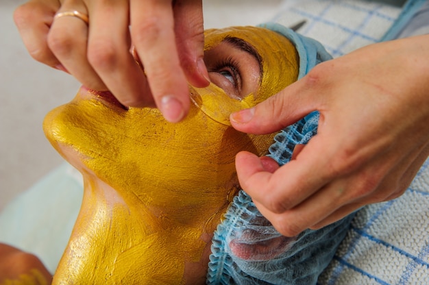 Beautiful woman with facial golden mask at beauty salon