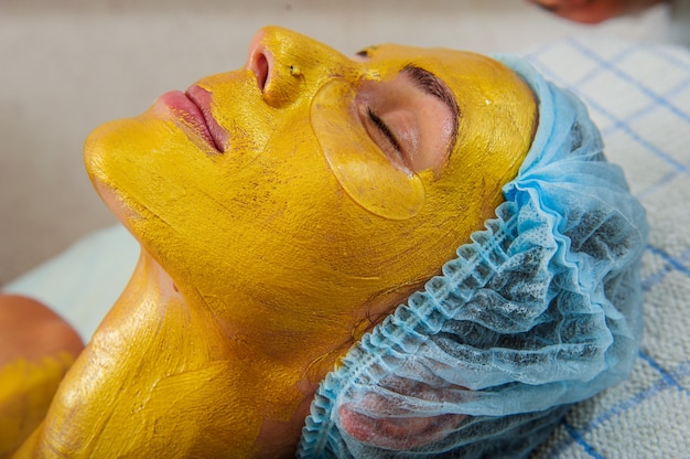 Beautiful woman with facial golden mask at beauty salon