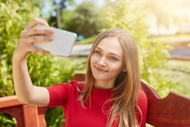 Selfieを作る赤いカジュアルセーターを着て金髪の美しい女性