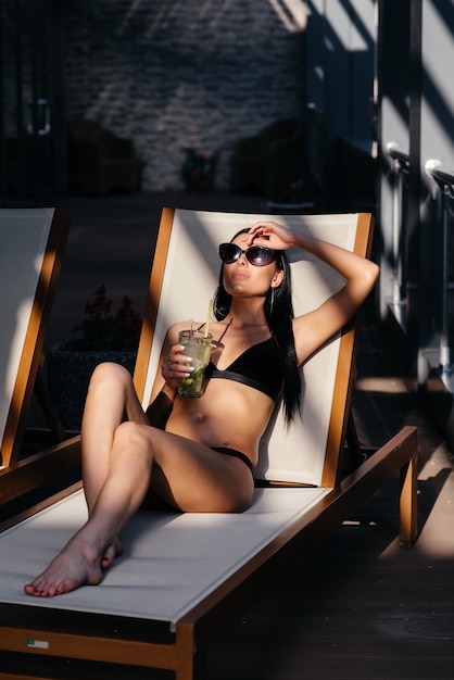 Beautiful woman with glamour make up in stylish black swimwear. Drink glass cocktail.
