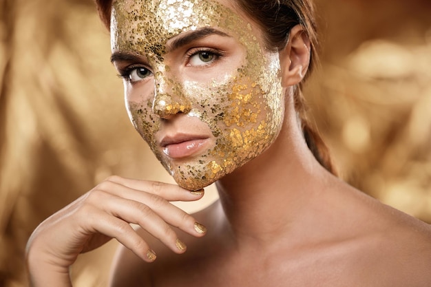 피부 치료를 위해 얼굴에 황금빛 빛나는 마스크를 쓴 아름다운 여성